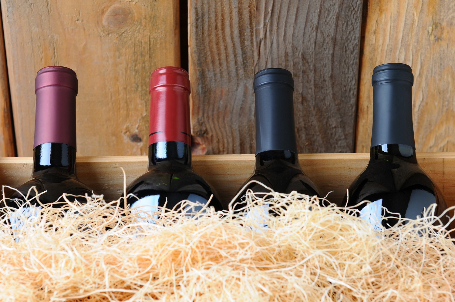 Closeup of four different wine bottles in a wooden crate with straw packing material.