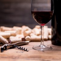 bottle of red wine, glass, wine corks, and corkscrew