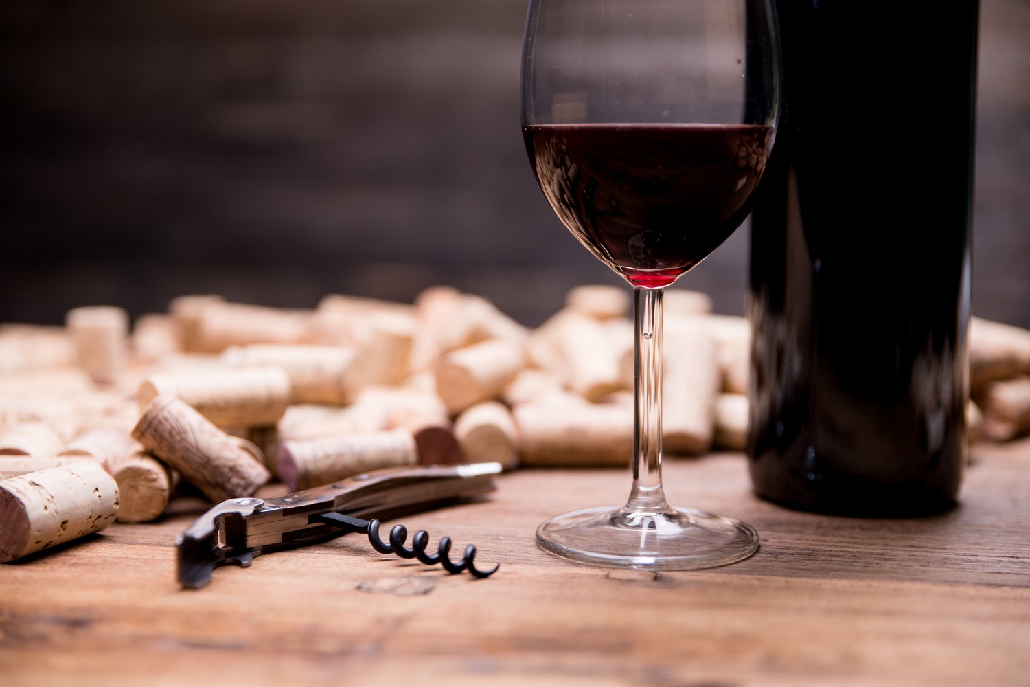 bottle of red wine, glass, wine corks, and corkscrew