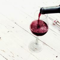 Pouring red wine from bottle in wine glass on vintage white wooden table with copyspace.